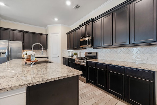 kitchen with a center island with sink, visible vents, light stone countertops, stainless steel appliances, and a sink