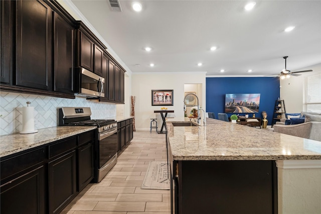 kitchen with stainless steel appliances, visible vents, a sink, and an island with sink