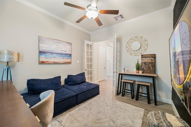 living room with light wood finished floors, baseboards, visible vents, ceiling fan, and crown molding