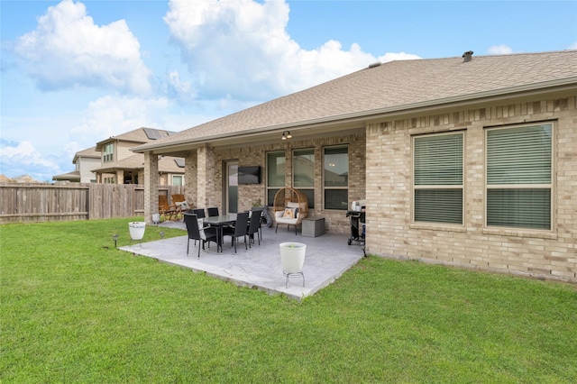 back of house featuring a patio area, roof with shingles, a lawn, and brick siding