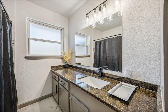 bathroom featuring marble finish floor, a textured wall, baseboards, and vanity