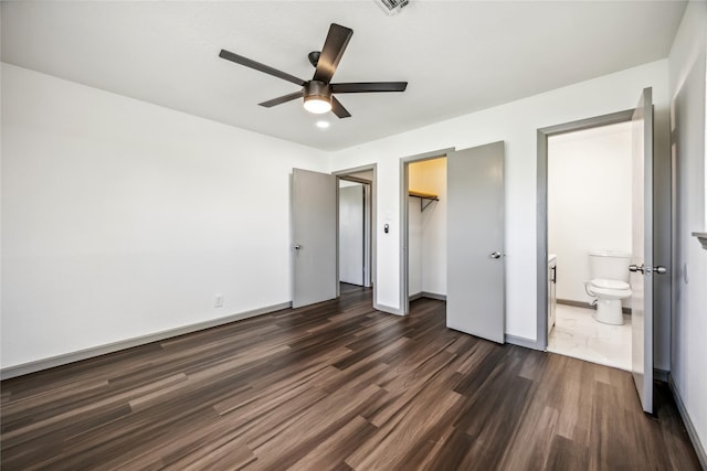 unfurnished bedroom with baseboards, dark wood-style floors, ensuite bathroom, a spacious closet, and a closet