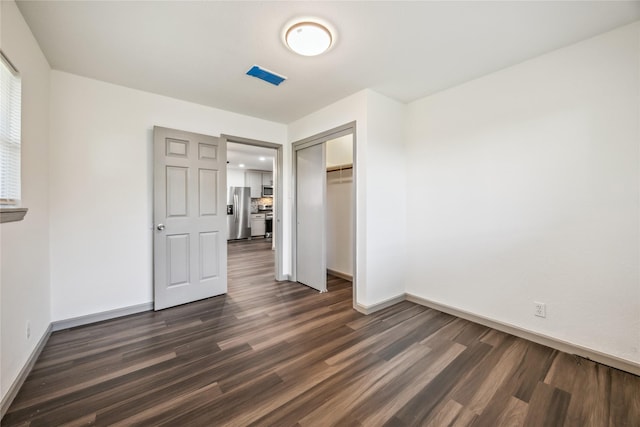 unfurnished bedroom featuring dark wood-style floors, a closet, stainless steel fridge, and baseboards