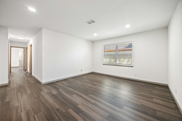 empty room featuring dark wood-type flooring, visible vents, and baseboards