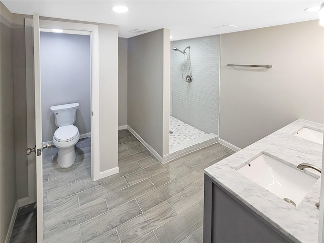 bathroom featuring double vanity, tiled shower, toilet, and baseboards