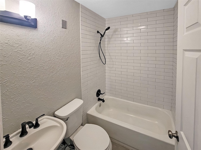 full bath with toilet, tub / shower combination, a sink, and a textured wall