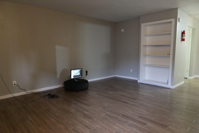 spare room with baseboards, wood finished floors, and built in features