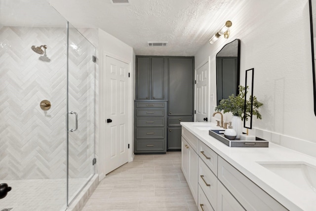 full bathroom featuring a textured ceiling, a sink, visible vents, a shower stall, and double vanity