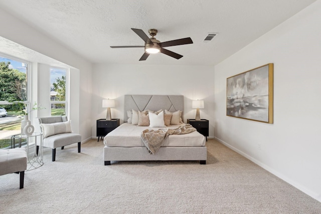 bedroom with visible vents, a ceiling fan, light carpet, a textured ceiling, and baseboards