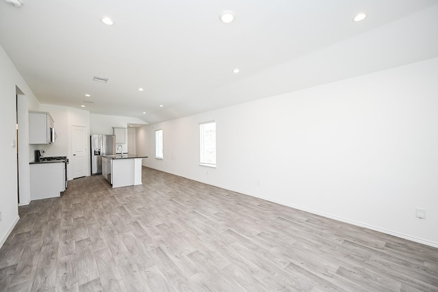 unfurnished living room featuring light wood finished floors, baseboards, a sink, and recessed lighting