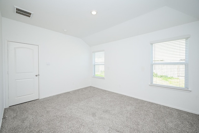 empty room featuring plenty of natural light, visible vents, vaulted ceiling, and carpet flooring