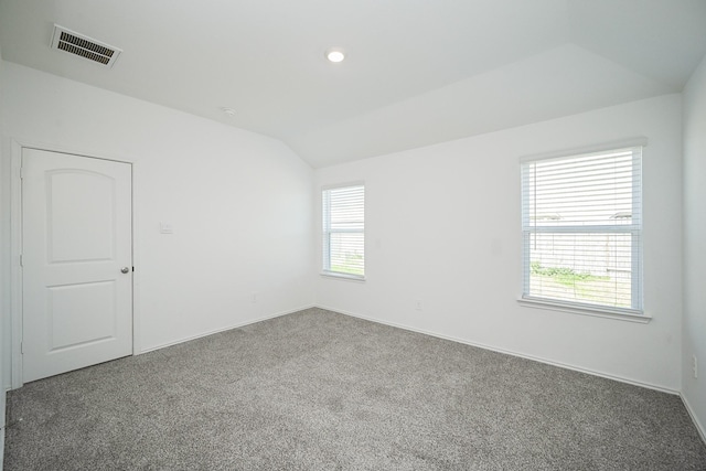 carpeted spare room with a wealth of natural light, visible vents, vaulted ceiling, and baseboards