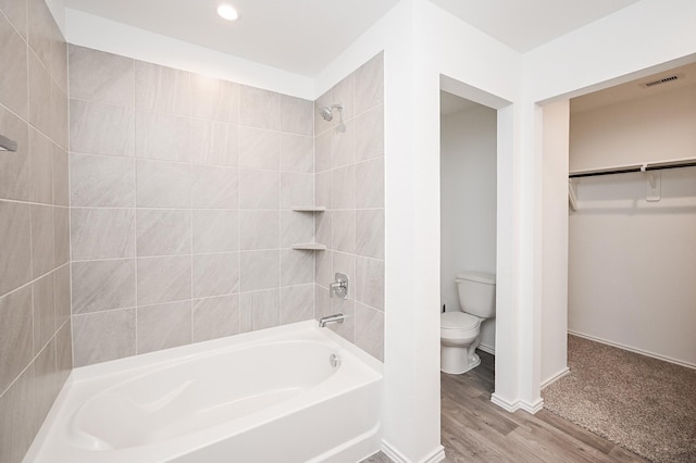 full bathroom with visible vents, toilet, wood finished floors, a walk in closet, and washtub / shower combination