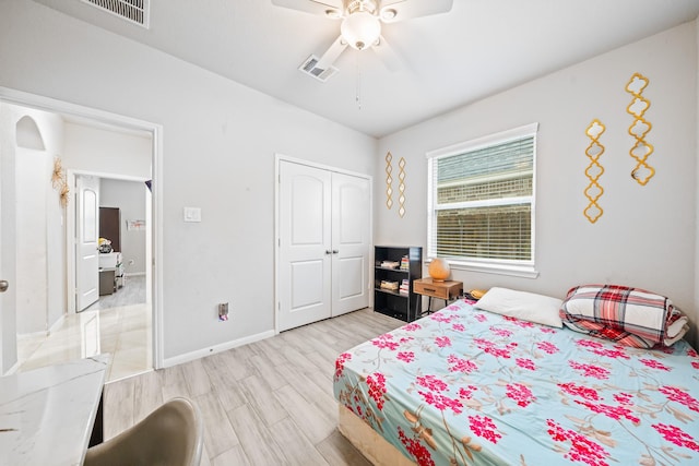 bedroom featuring ceiling fan, light wood-style flooring, visible vents, baseboards, and a closet