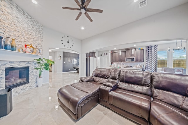 living room featuring arched walkways, a fireplace, visible vents, a ceiling fan, and vaulted ceiling