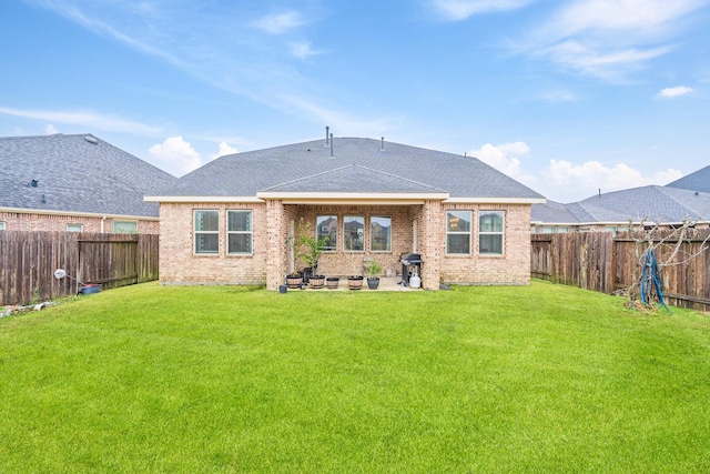 back of property with brick siding, a fenced backyard, a shingled roof, and a yard