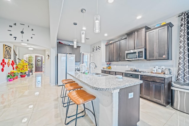 kitchen with arched walkways, a center island with sink, stainless steel appliances, backsplash, and a sink