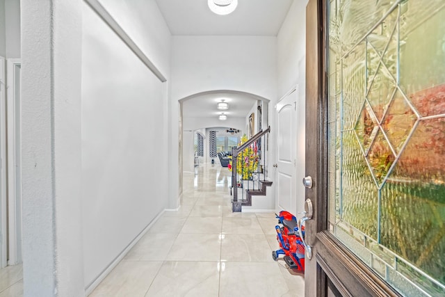 hallway featuring arched walkways, light tile patterned flooring, stairs, and baseboards