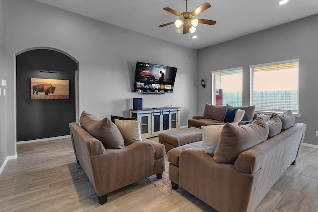 living room featuring baseboards, arched walkways, light wood-style flooring, ceiling fan, and recessed lighting