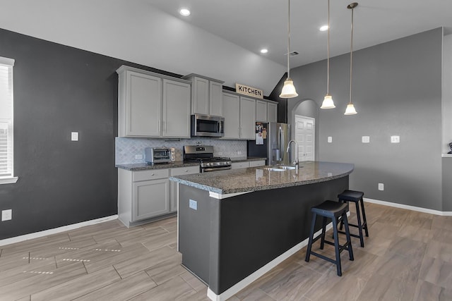 kitchen featuring arched walkways, gray cabinetry, a sink, appliances with stainless steel finishes, and backsplash