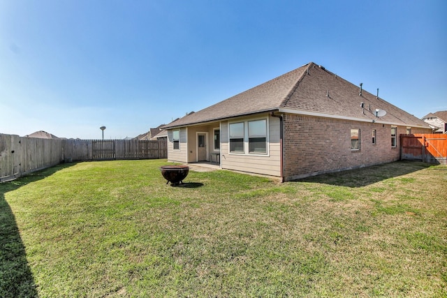 back of house with an outdoor fire pit, a shingled roof, a lawn, a fenced backyard, and brick siding