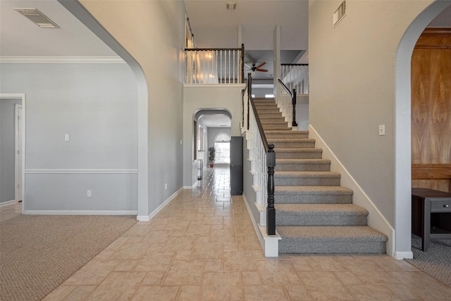 carpeted foyer entrance featuring arched walkways, visible vents, stairway, and baseboards