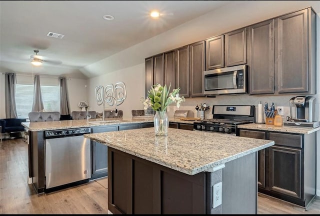 kitchen with stainless steel appliances, a peninsula, a kitchen island, visible vents, and dark brown cabinets