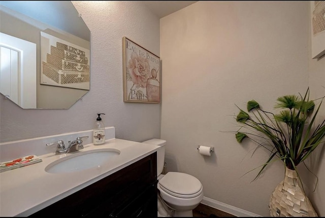 half bathroom with toilet, vanity, and baseboards