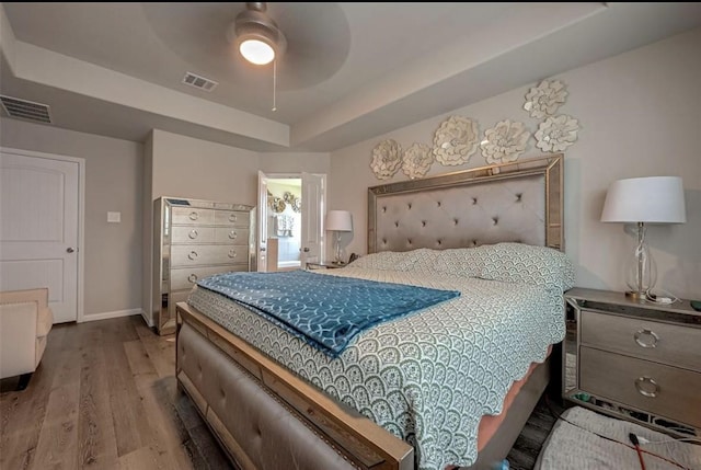 bedroom featuring baseboards, visible vents, a tray ceiling, and wood finished floors