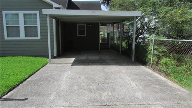 view of parking / parking lot featuring driveway, a carport, and fence