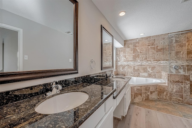 full bathroom with double vanity, visible vents, a garden tub, a textured ceiling, and a sink