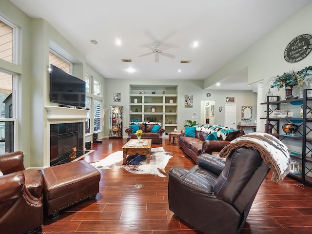 living area featuring visible vents, dark wood-style floors, ceiling fan, built in shelves, and a fireplace