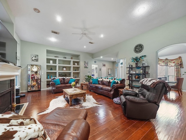 living room featuring arched walkways, built in shelves, a fireplace, visible vents, and dark wood-style floors