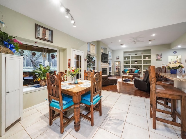 dining area featuring built in shelves, light tile patterned flooring, a fireplace, and a ceiling fan