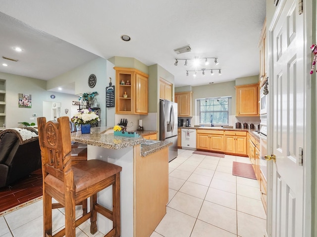 kitchen with a breakfast bar, white dishwasher, a sink, stainless steel fridge, and a peninsula