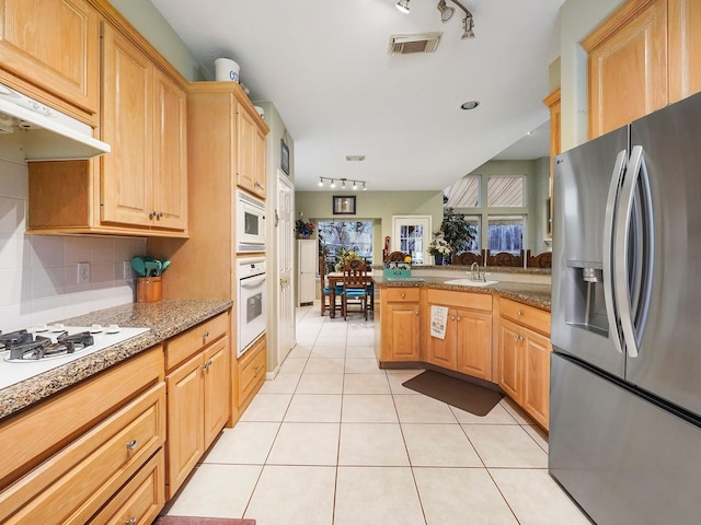 kitchen with light tile patterned floors, under cabinet range hood, white appliances, a sink, and visible vents