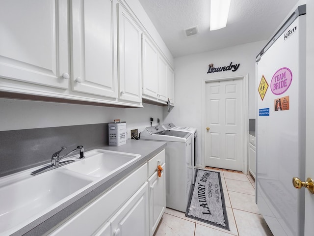 clothes washing area featuring washing machine and clothes dryer, light tile patterned floors, cabinet space, a sink, and a textured ceiling