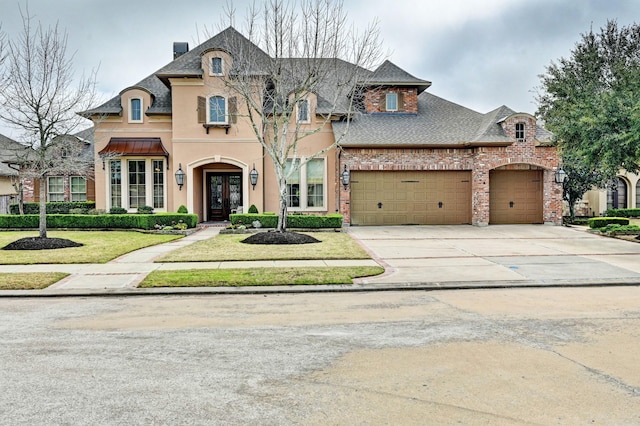 french country inspired facade with a front lawn, concrete driveway, brick siding, and an attached garage