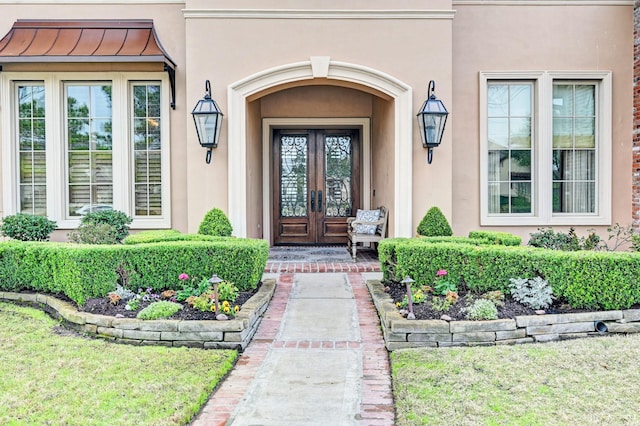 view of exterior entry with french doors, metal roof, a standing seam roof, and stucco siding