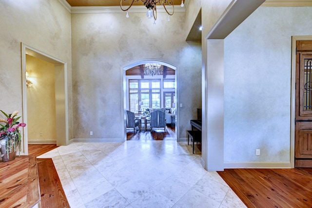 entryway featuring arched walkways, ornamental molding, a high ceiling, and baseboards