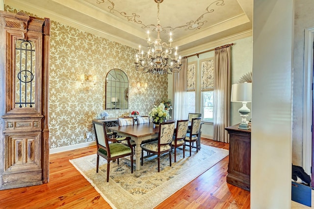 dining space featuring a tray ceiling, crown molding, wood finished floors, baseboards, and wallpapered walls