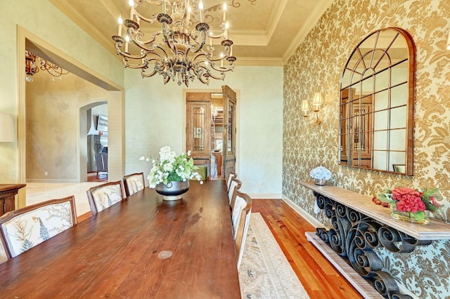 dining space featuring arched walkways, crown molding, a raised ceiling, wood finished floors, and a chandelier