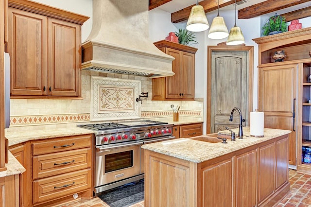 kitchen with range with two ovens, pendant lighting, custom exhaust hood, a sink, and an island with sink