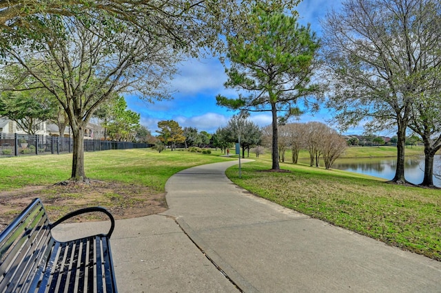 surrounding community with a lawn, a water view, and fence