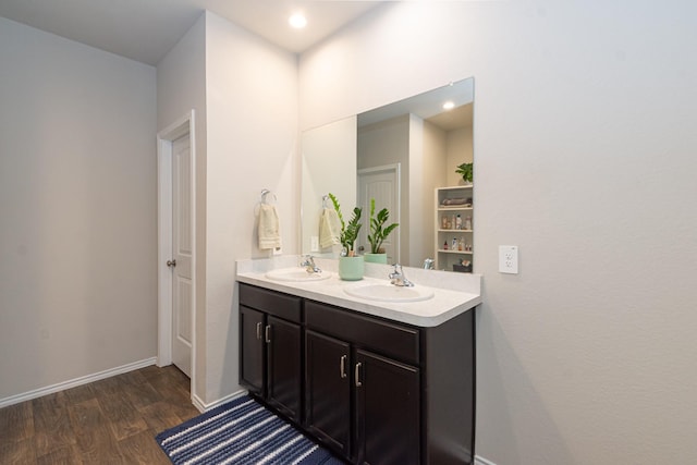 full bath featuring double vanity, a sink, baseboards, and wood finished floors