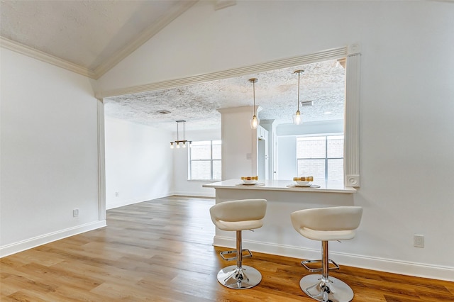 kitchen featuring a breakfast bar area, decorative light fixtures, vaulted ceiling, baseboards, and light wood finished floors