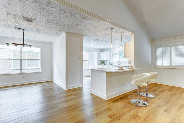 kitchen with ornamental molding, a peninsula, a breakfast bar, light wood-type flooring, and a sink