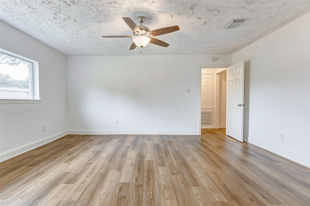 spare room with a ceiling fan, light wood finished floors, a textured ceiling, and visible vents