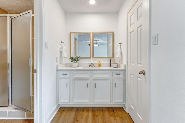bathroom featuring vanity, wood finished floors, baseboards, ceiling fan, and a stall shower