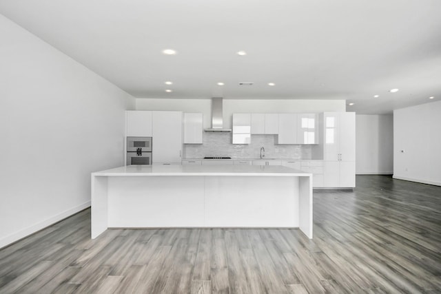 kitchen with a kitchen island, wall chimney exhaust hood, modern cabinets, and white cabinetry